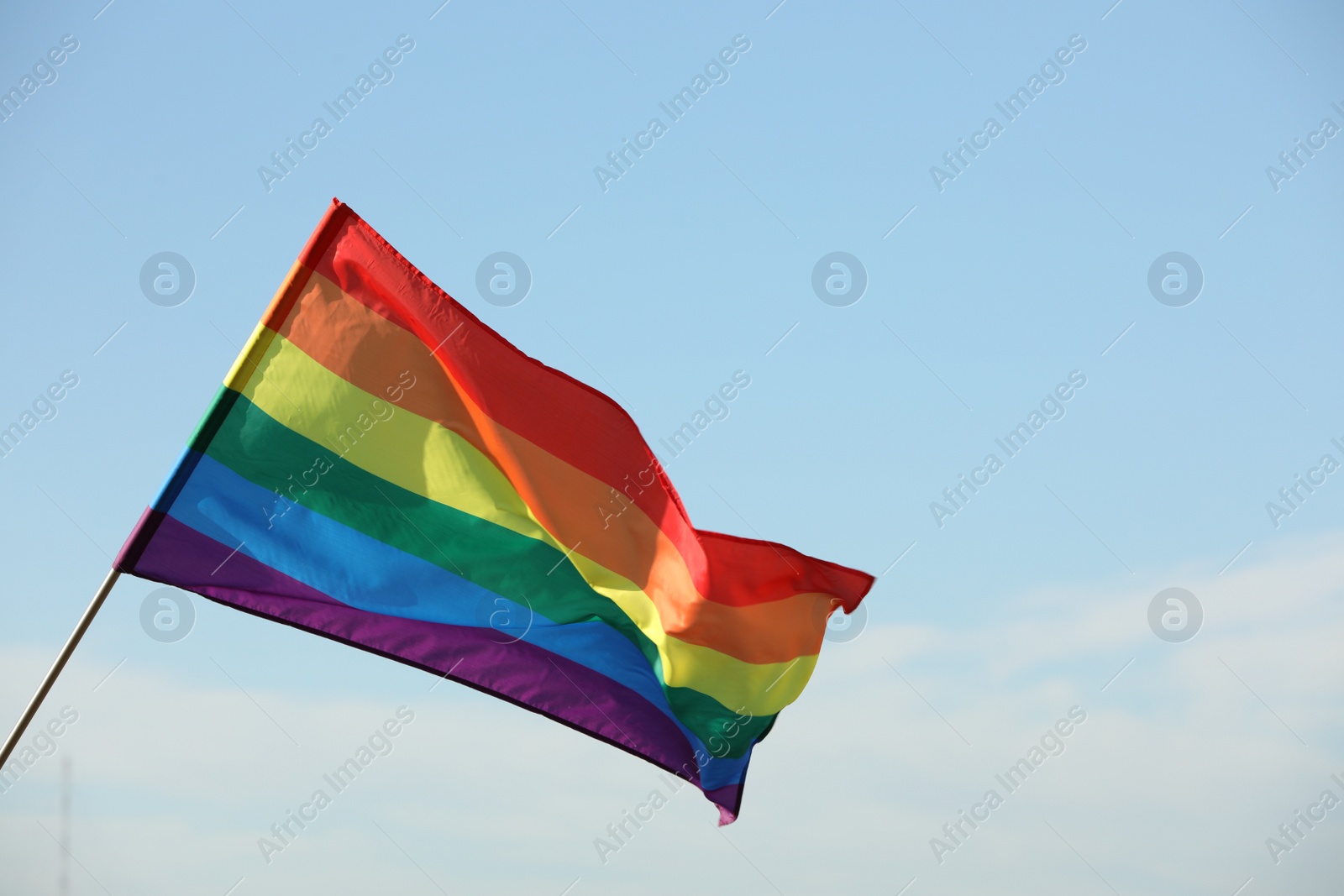 Photo of Bright LGBT flag against blue sky with clouds, space for text