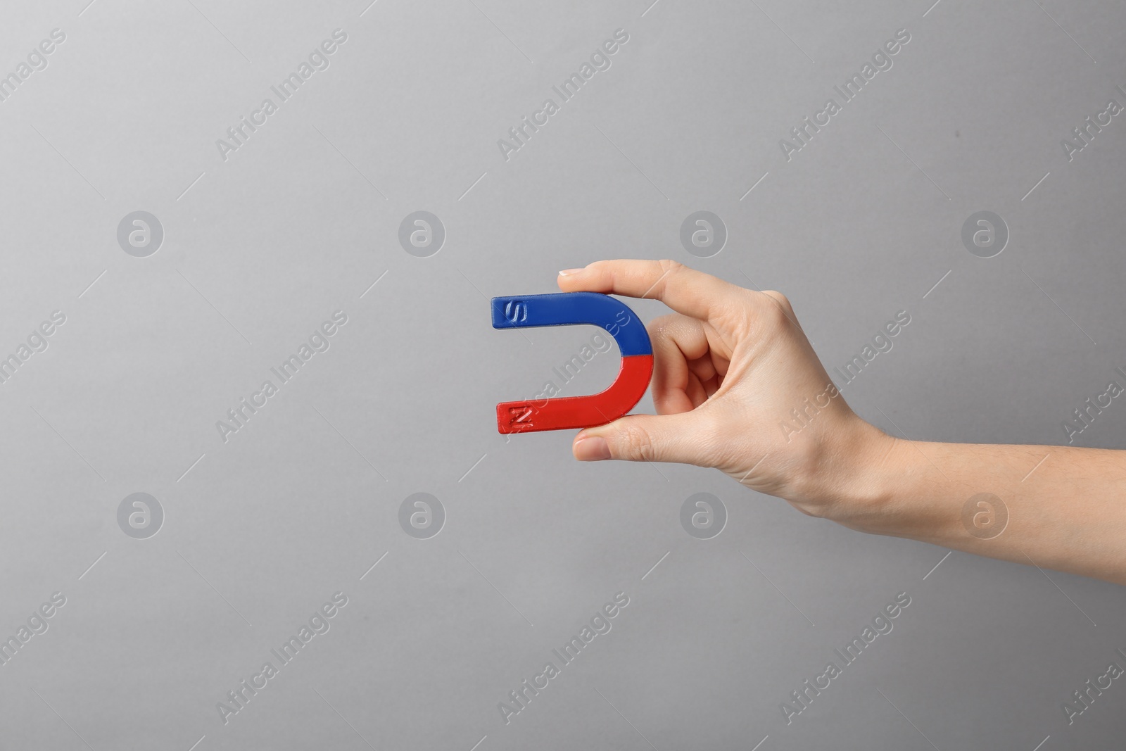 Photo of Woman holding magnet on grey background, closeup. Space for text