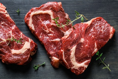 Photo of Flat lay composition with fresh meat steaks on black wooden table