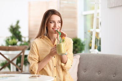 Photo of Young woman with tasty healthy smoothie at table, indoors