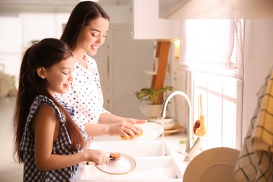 Photo of Mother and daughter washing dishes together in kitchen