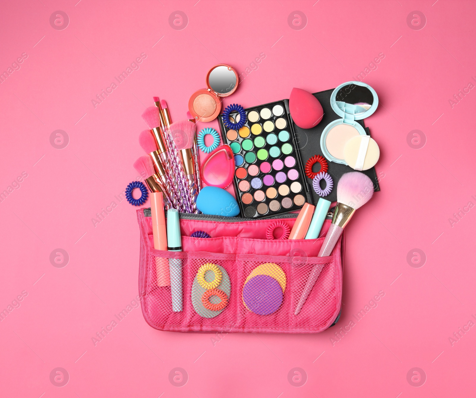 Photo of Cosmetic bag with makeup products and beauty accessories on pink background, flat lay