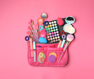 Photo of Cosmetic bag with makeup products and beauty accessories on pink background, flat lay