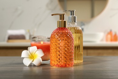 Photo of Glass dispensers with liquid soap, plumeria flower and candle on wooden table in bathroom