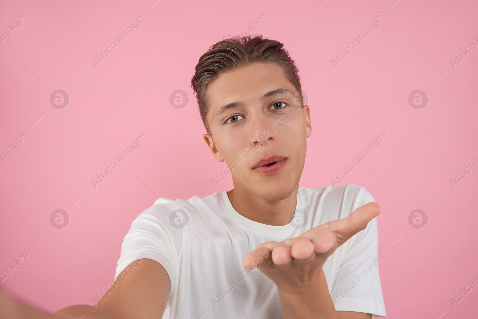 Photo of Handsome man taking selfie and blowing kiss on pink background