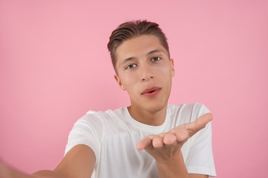 Handsome man taking selfie and blowing kiss on pink background