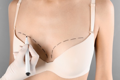 Photo of Doctor drawing marks on patient's breast for cosmetic surgery operation against gray background, closeup