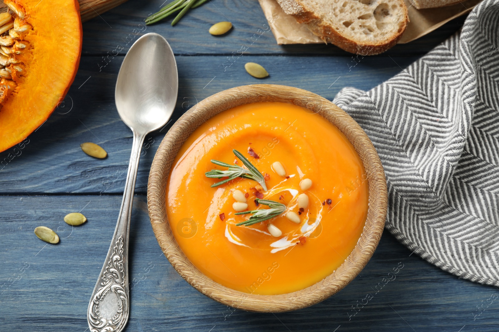 Photo of Delicious pumpkin soup in bowl on blue wooden table, flat lay