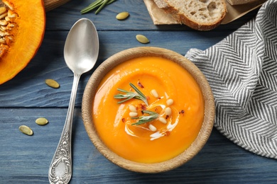 Photo of Delicious pumpkin soup in bowl on blue wooden table, flat lay