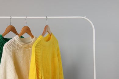 Photo of Rack with different warm sweaters on light grey background. Space for text