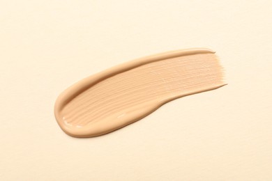 Photo of Smear of skin foundation on beige background, top view