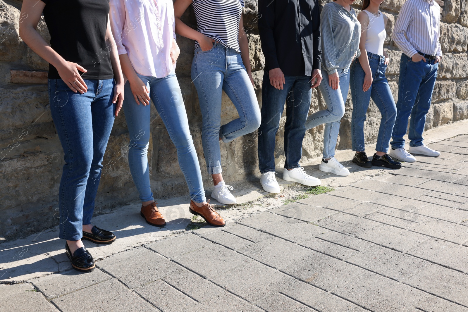 Photo of Group of people in stylish jeans near stone wall outdoors on sunny day, closeup