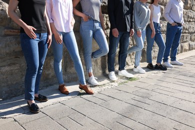 Photo of Group of people in stylish jeans near stone wall outdoors on sunny day, closeup