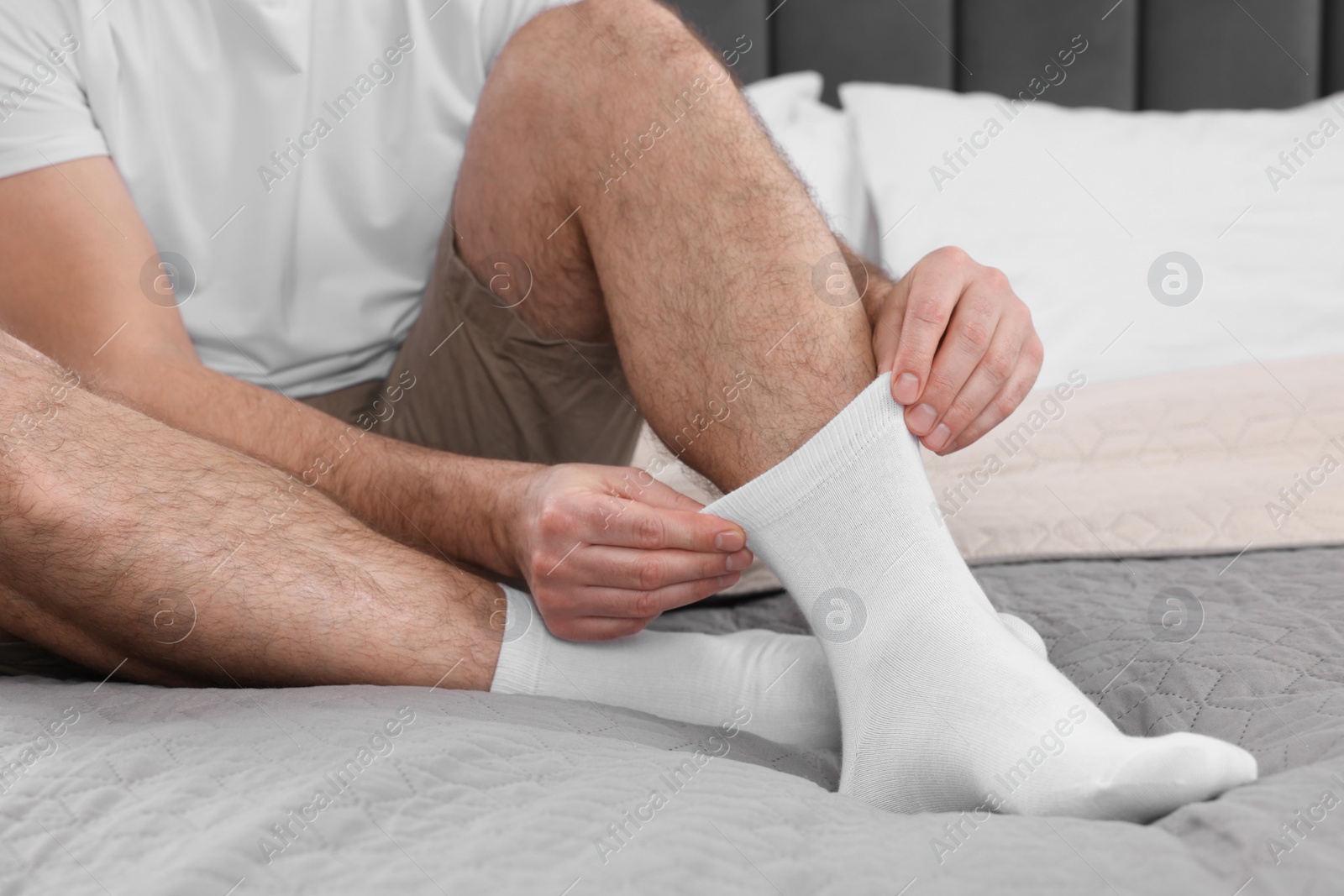 Photo of Man putting on white socks at home, closeup