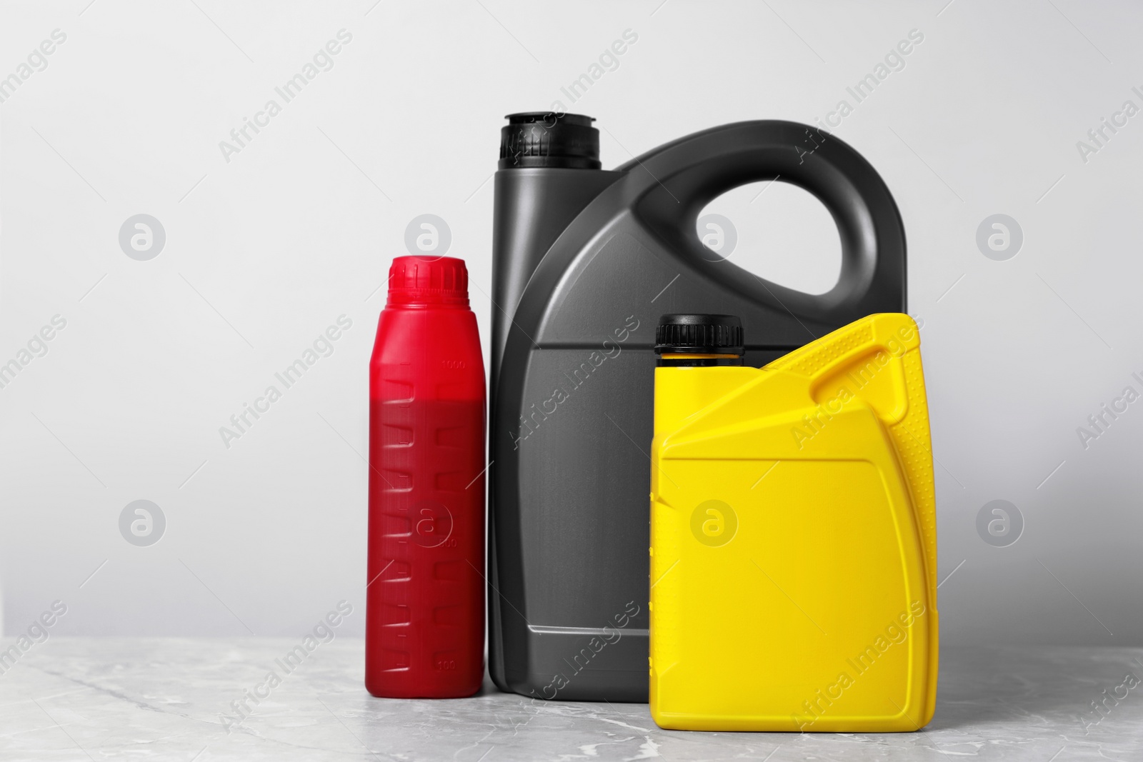 Photo of Motor oil in different canisters on grey marble table against light background