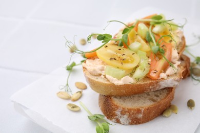 Tasty vegan sandwich with tomatoes, celery and microgreens on white tiled table, closeup