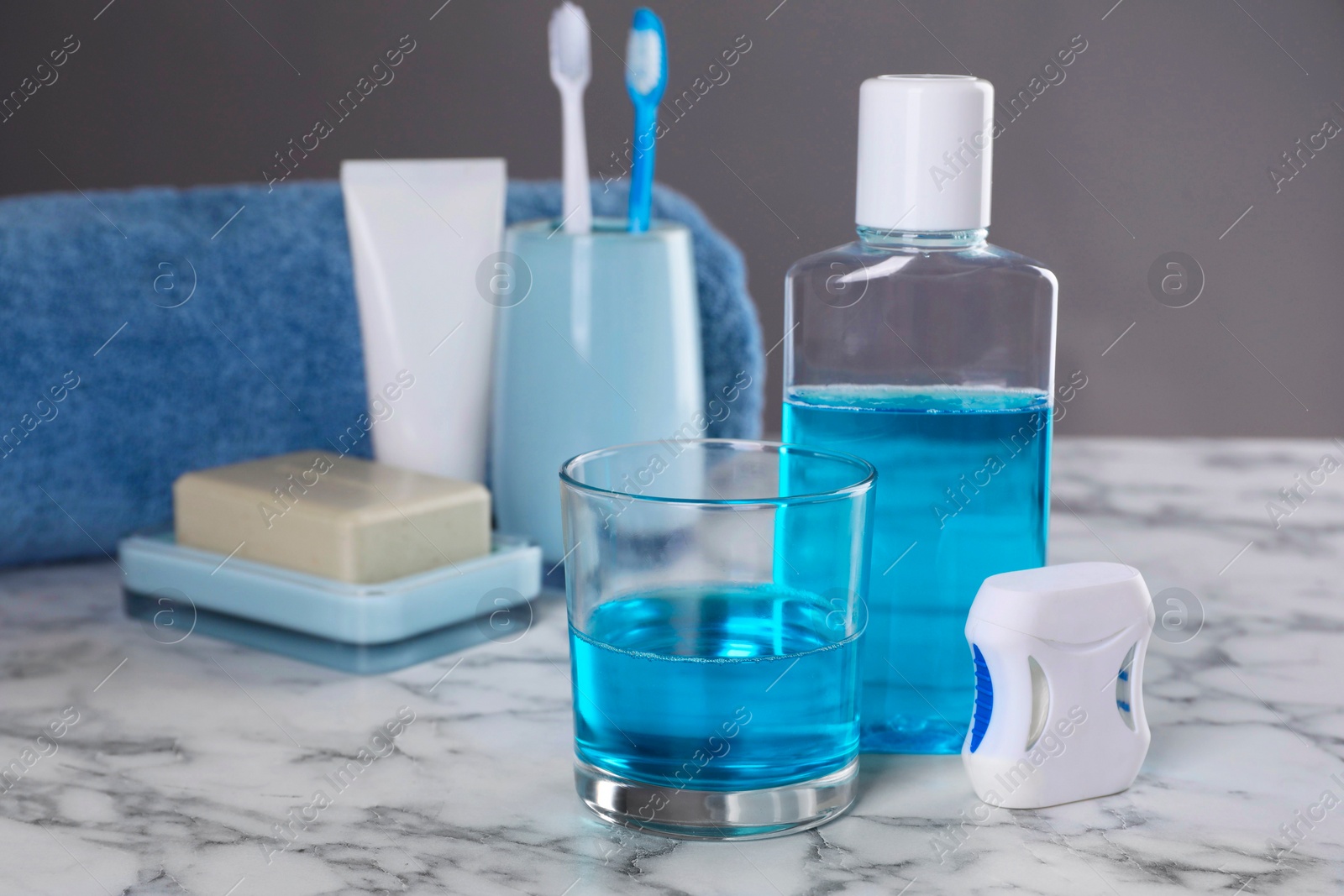 Photo of Fresh mouthwash in bottle, glass and dental floss on white marble table. Space for text
