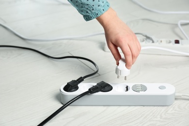 Woman inserting power plug into extension cord on floor, closeup with space for text. Electrician's professional equipment