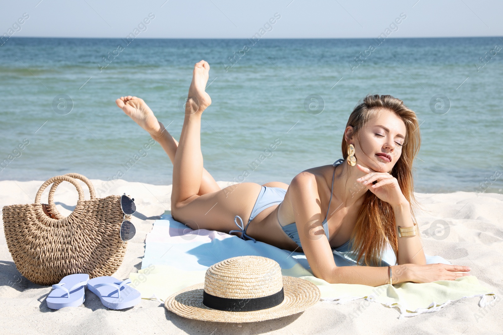 Photo of Beautiful woman with bag and other beach stuff on sand near sea