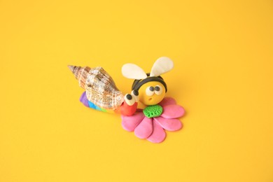Photo of Bee with flower and snail made from plasticine on orange background. Children's handmade ideas