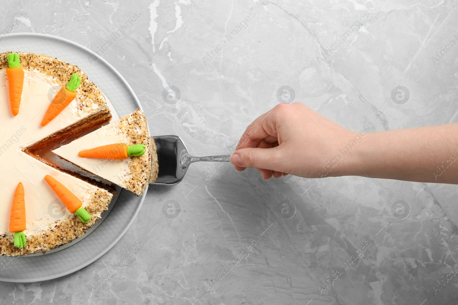 Photo of Woman taking piece of sweet carrot cake with delicious cream at grey marble table, top view