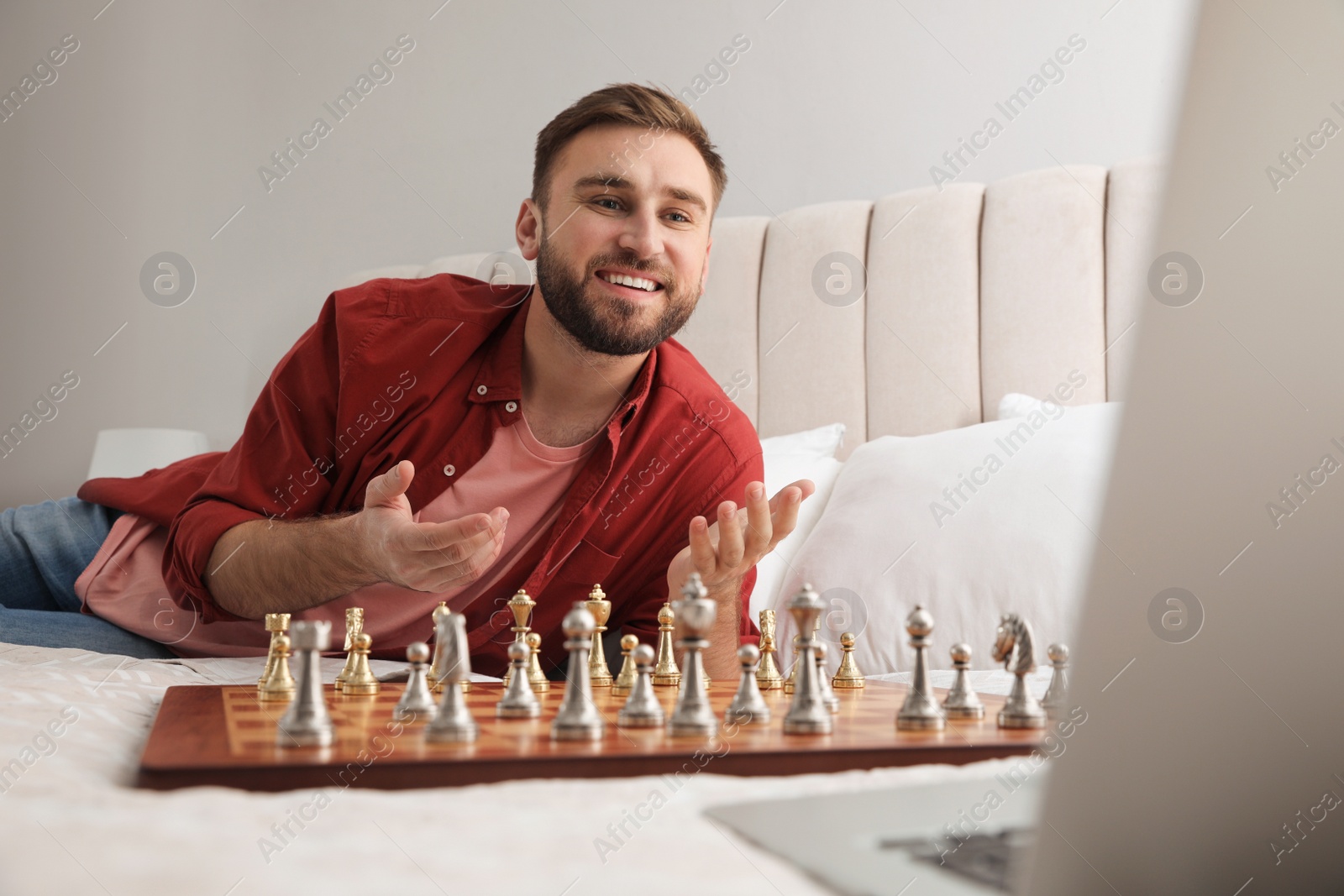 Photo of Young man playing chess with partner through online video chat on bed at home