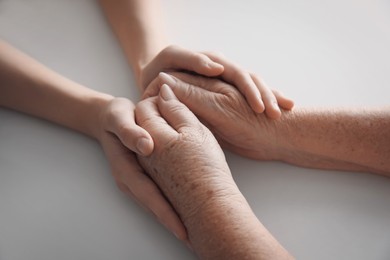 Photo of Young and elderly women holding hands together at white table, closeup