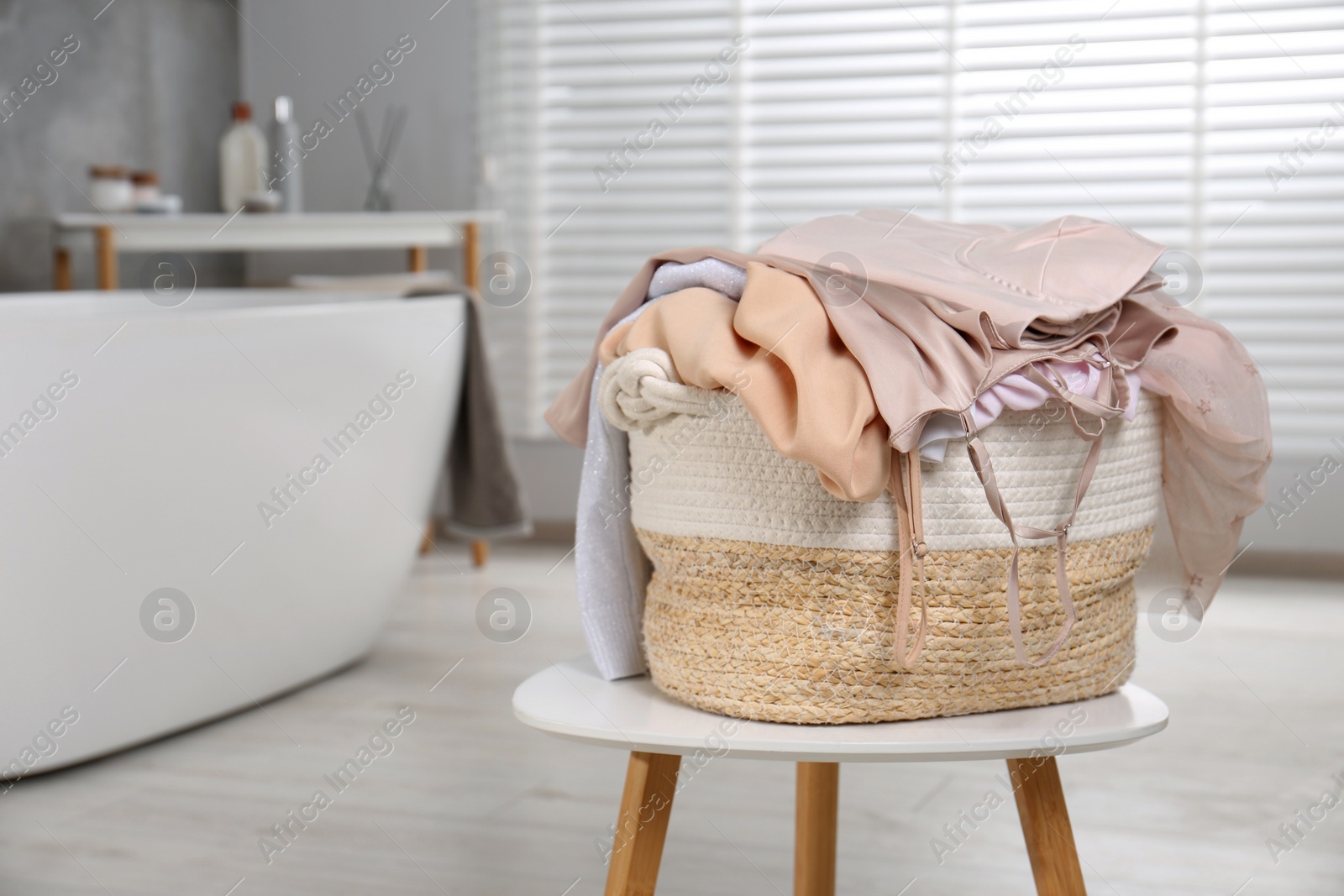Photo of Wicker laundry basket with clothes on stool in bathroom
