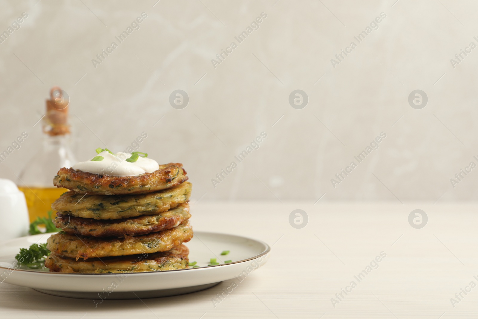 Photo of Delicious zucchini pancakes with sour cream served on white wooden table. Space for text