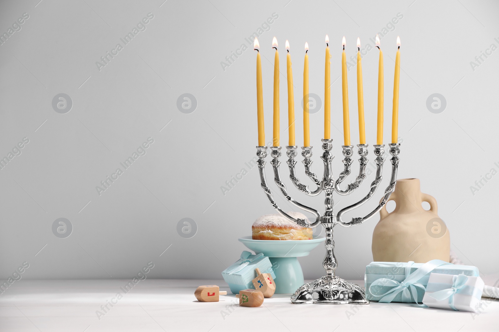 Photo of Hanukkah celebration. Menorah with burning candles, dreidels and gift boxes on white table, space for text