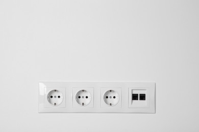 Photo of Many power sockets with ethernet plate on white wall indoors. Space for text