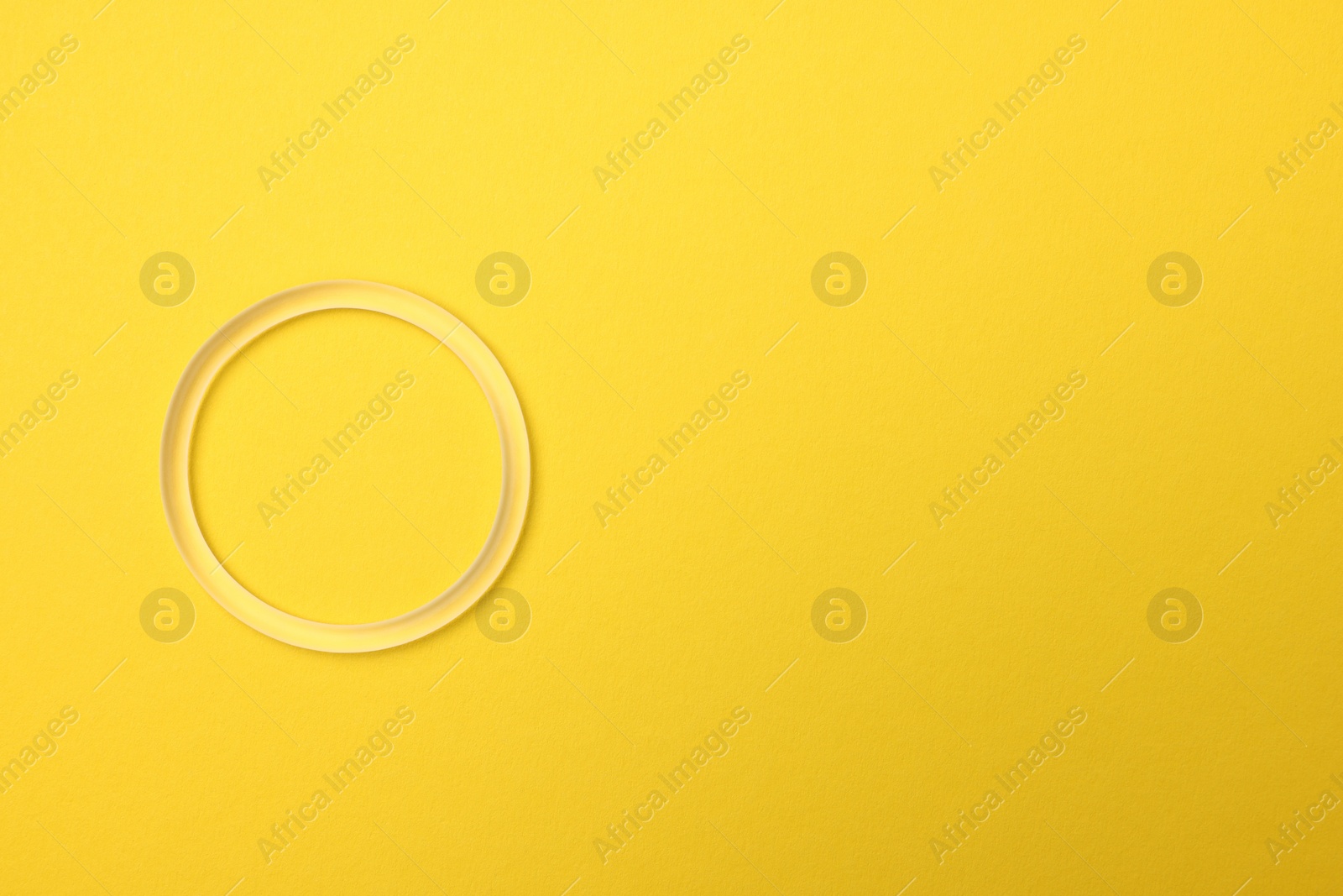 Photo of Diaphragm vaginal contraceptive ring on yellow background, top view. Space for text