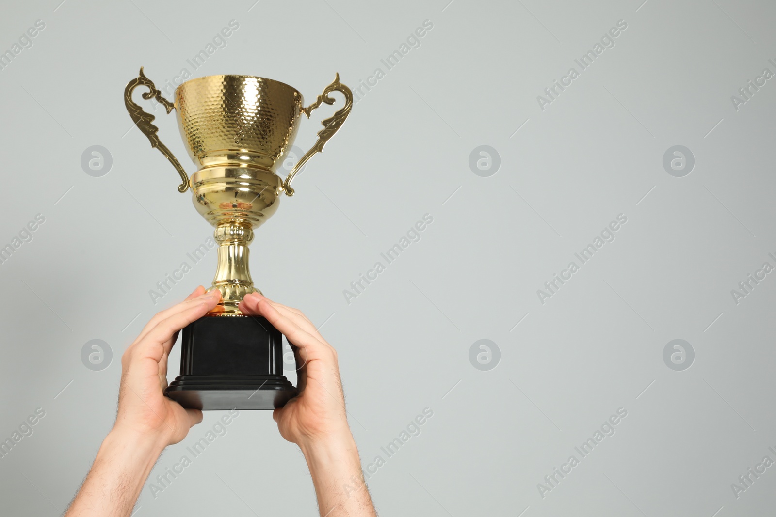 Photo of Man holding gold trophy cup on light grey background, closeup. Space for text