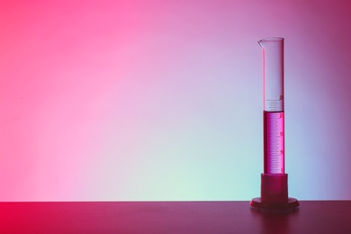 Photo of Graduated cylinder with liquid on table against color background. Chemistry laboratory glassware