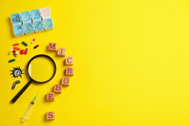 Photo of Word Microbes made with wooden cubes, pill box, syringe and magnifying glass on yellow background, flat lay. Space for text