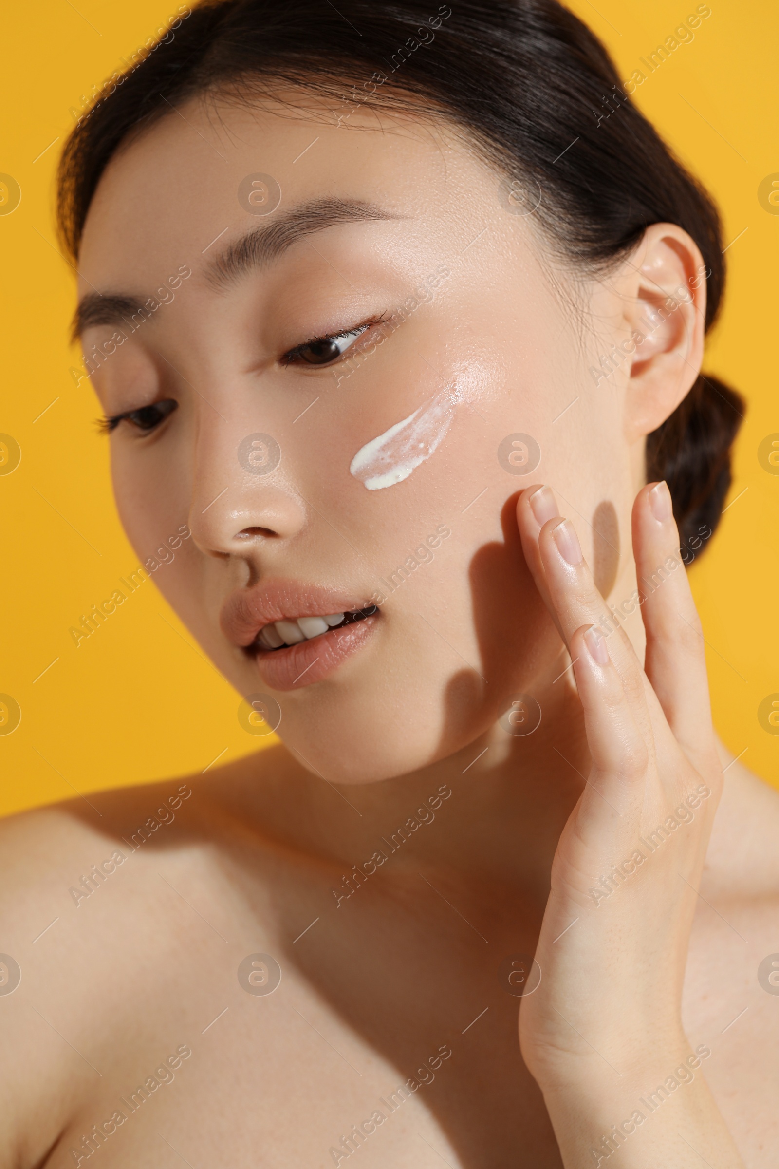 Photo of Beautiful young woman with sun protection cream on her face against orange background