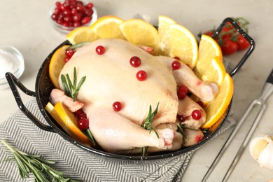 Photo of Chicken with orange slices, red berries and rosemary in round baking pan on light grey table