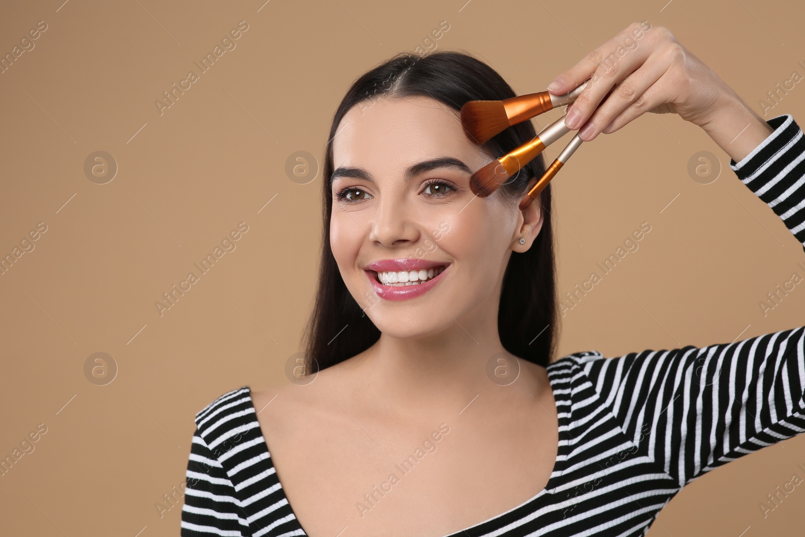 Photo of Happy woman with different makeup brushes on light brown background