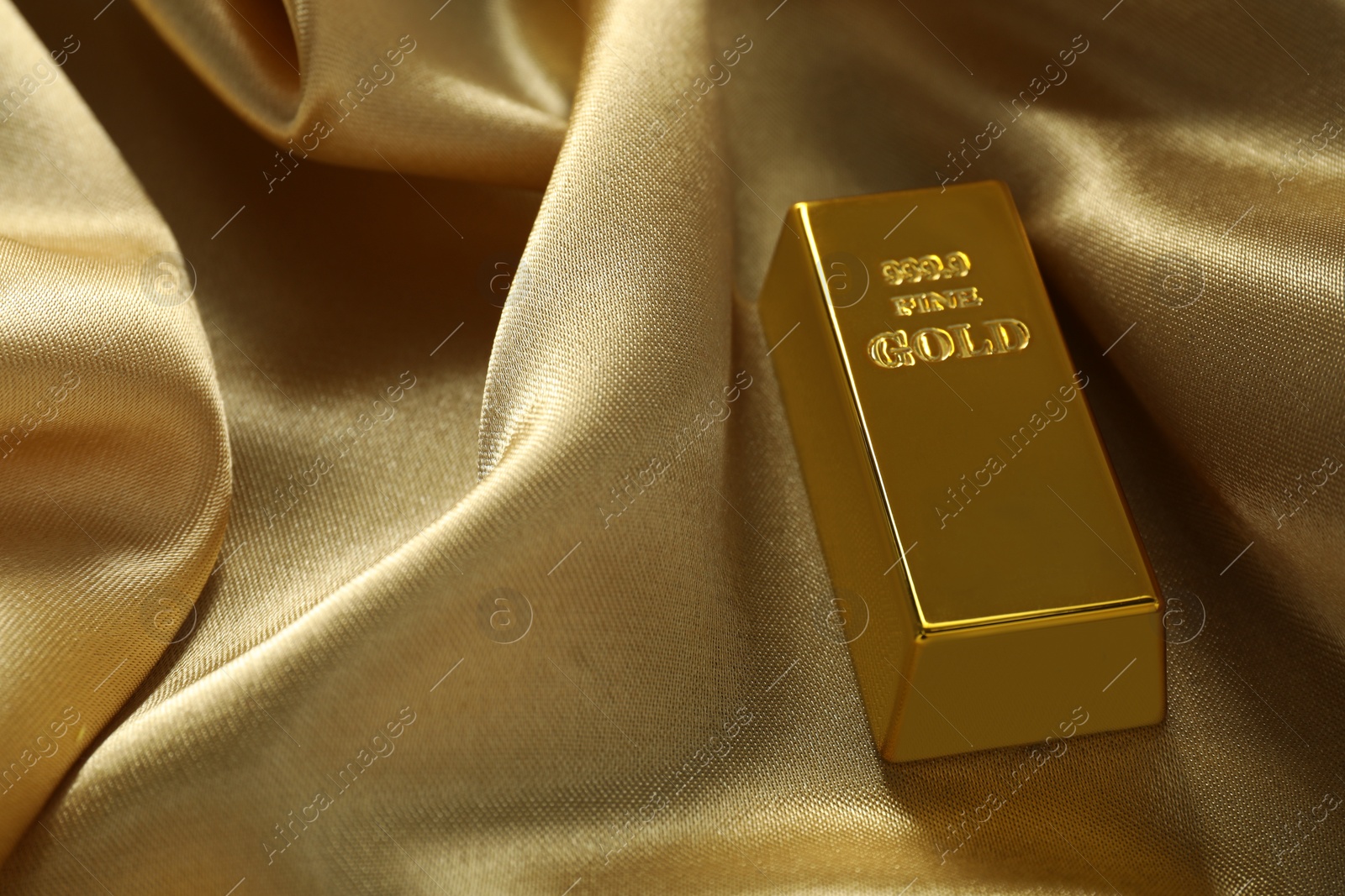 Photo of Gold bar on shiny silk fabric, closeup. Space for text
