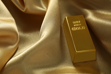 Photo of Gold bar on shiny silk fabric, closeup. Space for text