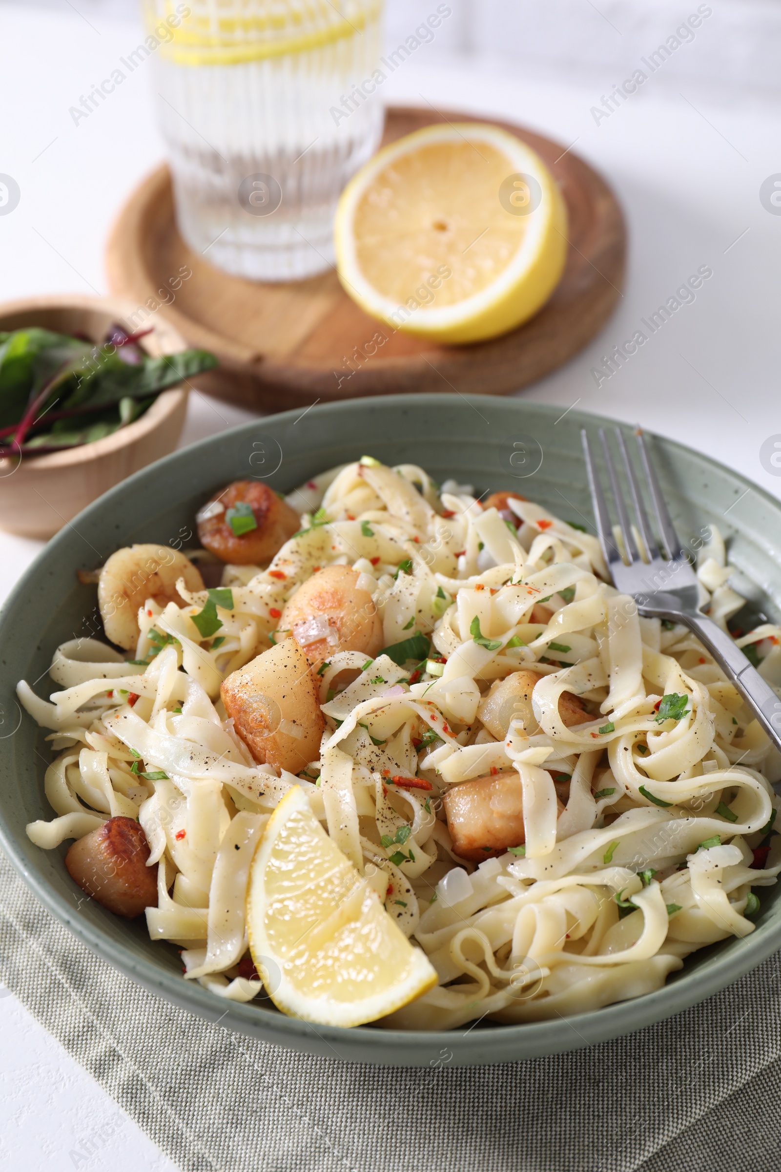 Photo of Delicious scallop pasta with spices and lemon in bowl served on white table, closeup