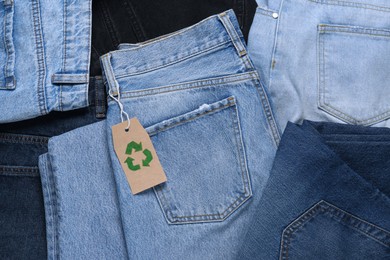 Photo of Different jeans with recycling label as background, top view