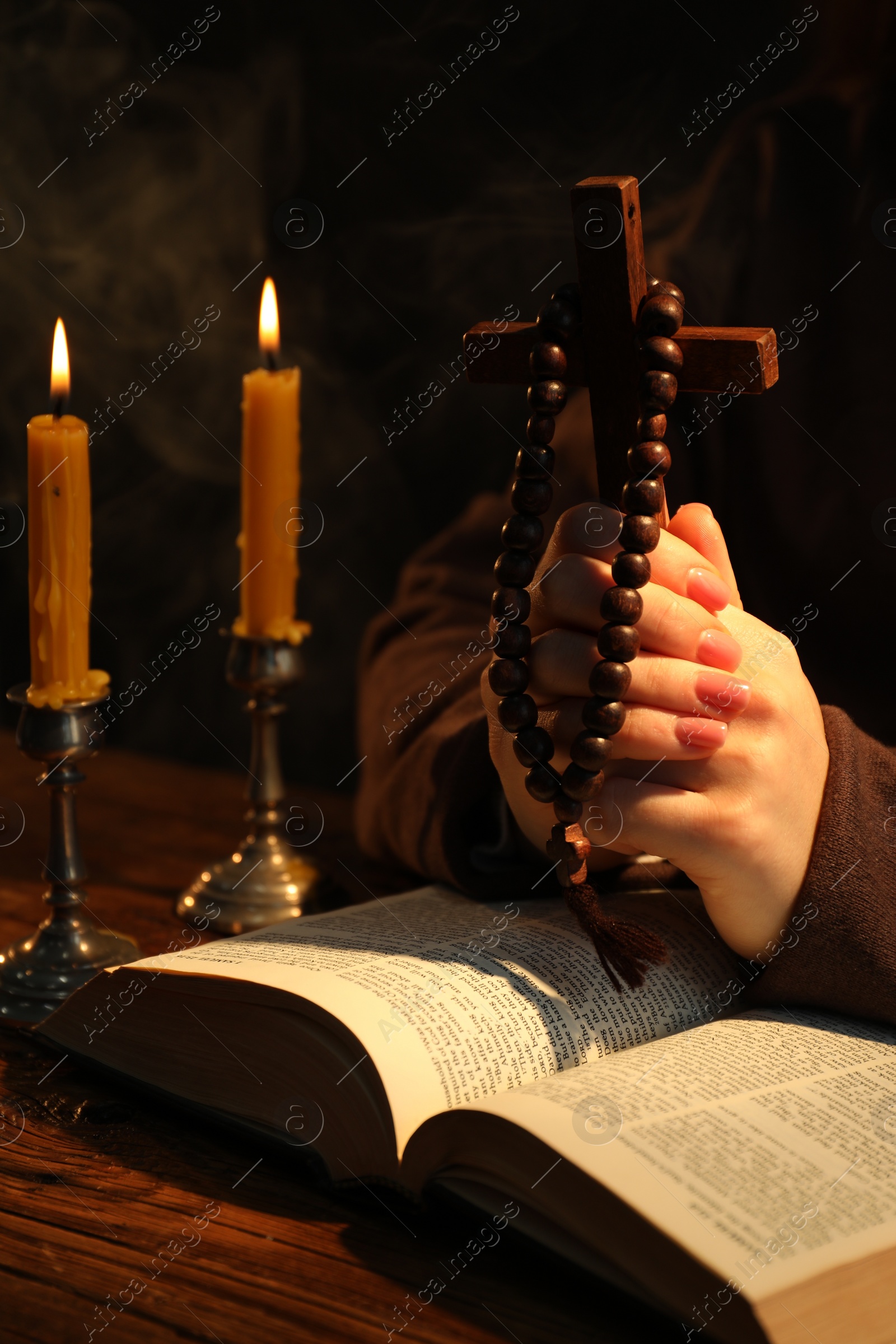 Photo of Woman praying at table with burning candles and Bible, closeup