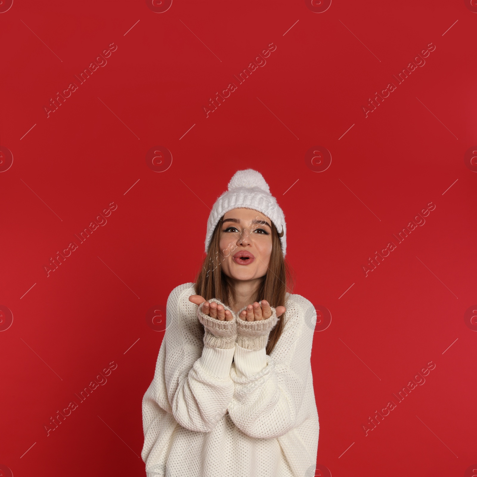 Photo of Beautiful young woman in white sweater and hat on red background. Winter season