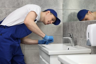 Photo of Smiling plumber wearing gloves examining faucet in bathroom