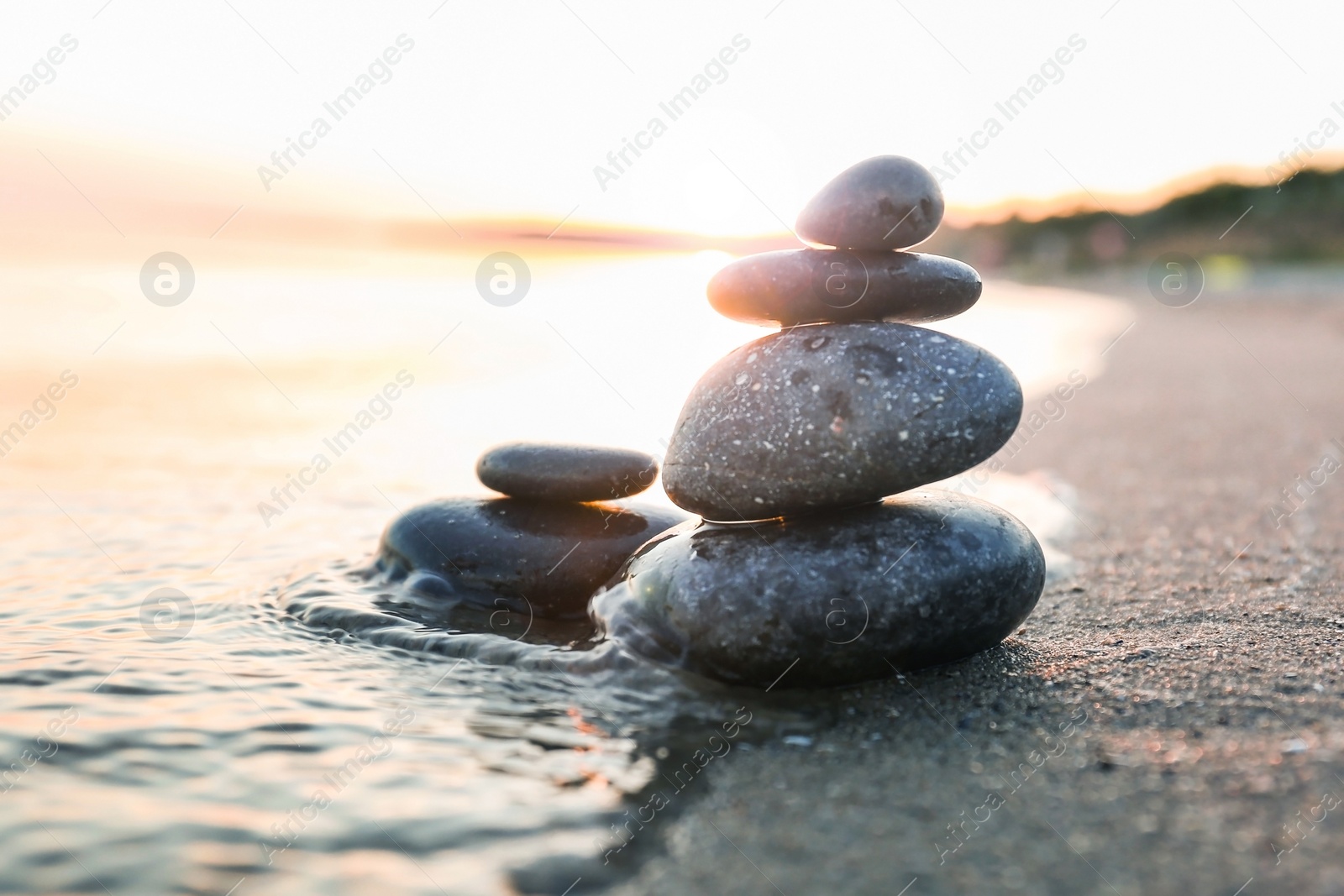 Photo of Dark stones on sand near sea at sunset. Zen concept