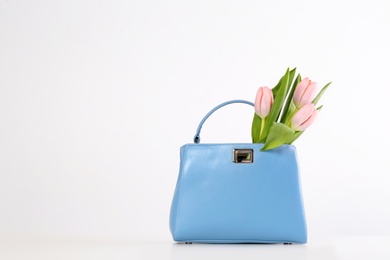 Photo of Stylish woman's handbag and spring flowers on light background