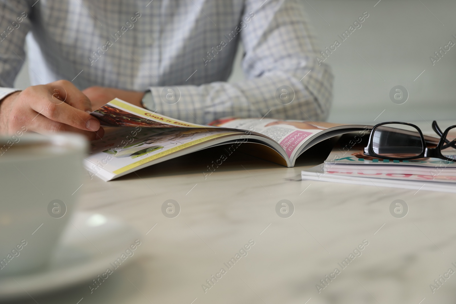 Photo of Man reading magazine at white table, closeup