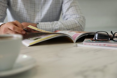 Photo of Man reading magazine at white table, closeup