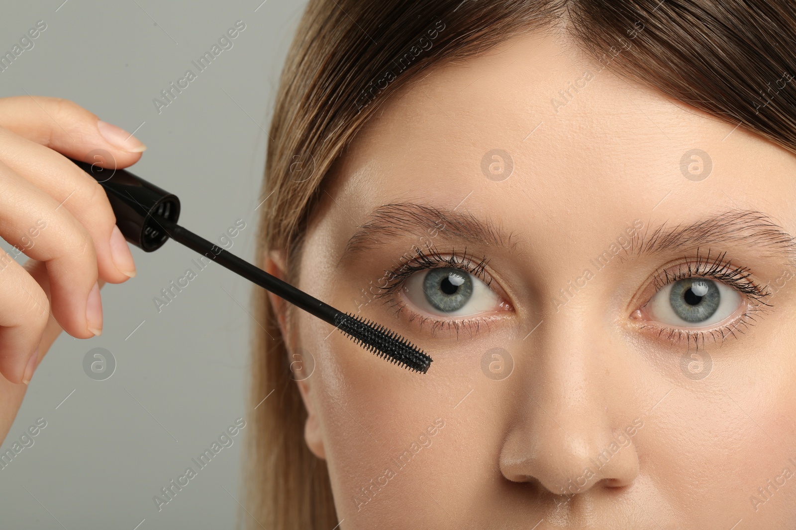 Photo of Woman applying mascara onto eyelashes against grey background, closeup